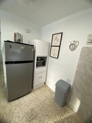 Eine kleine Küche mit Kühlschrank, Mikrowelle und Mülleimer.