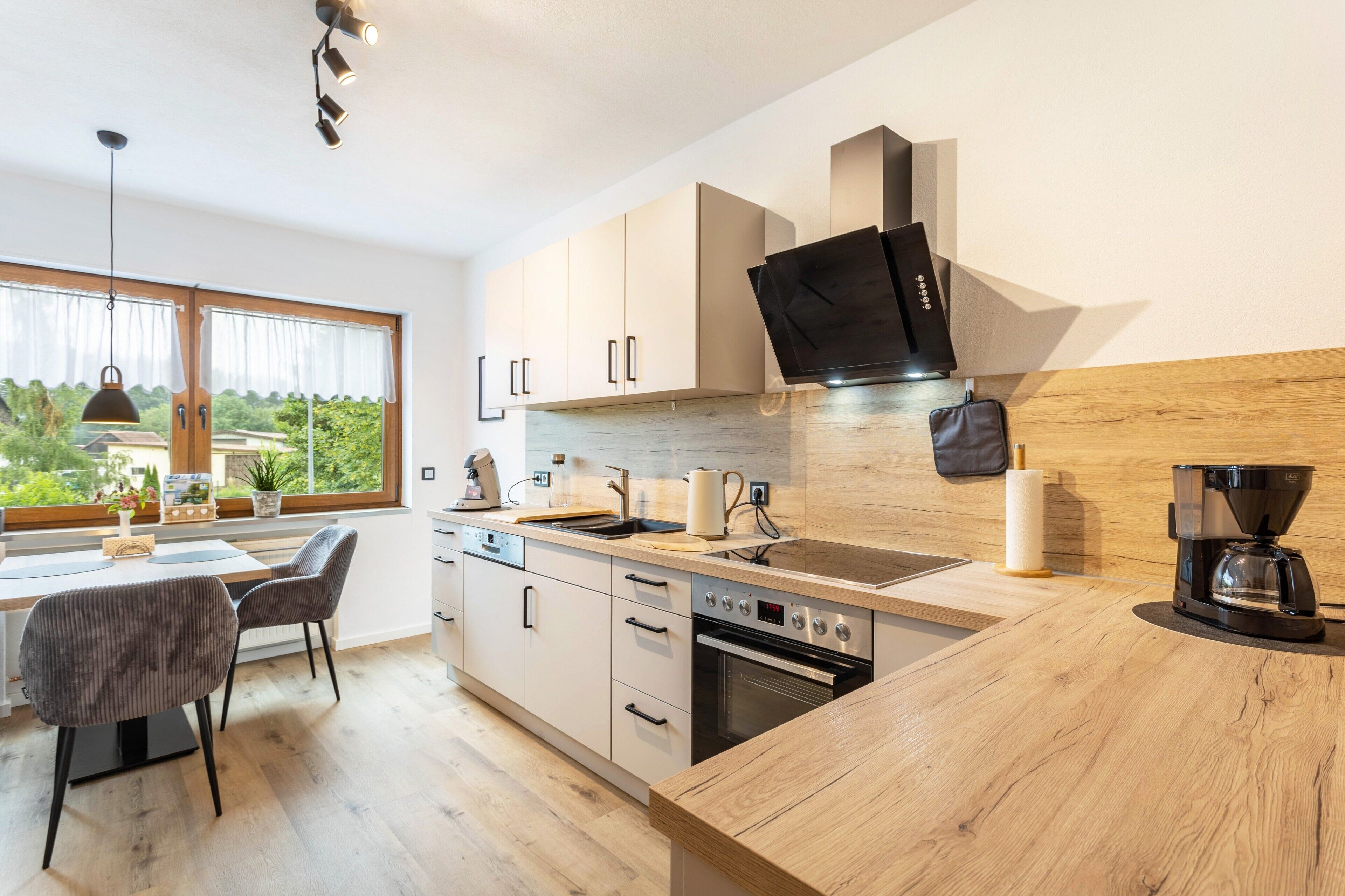 A modern kitchen with a large window, wooden cabinets, a built-in oven, and a coffee maker.
