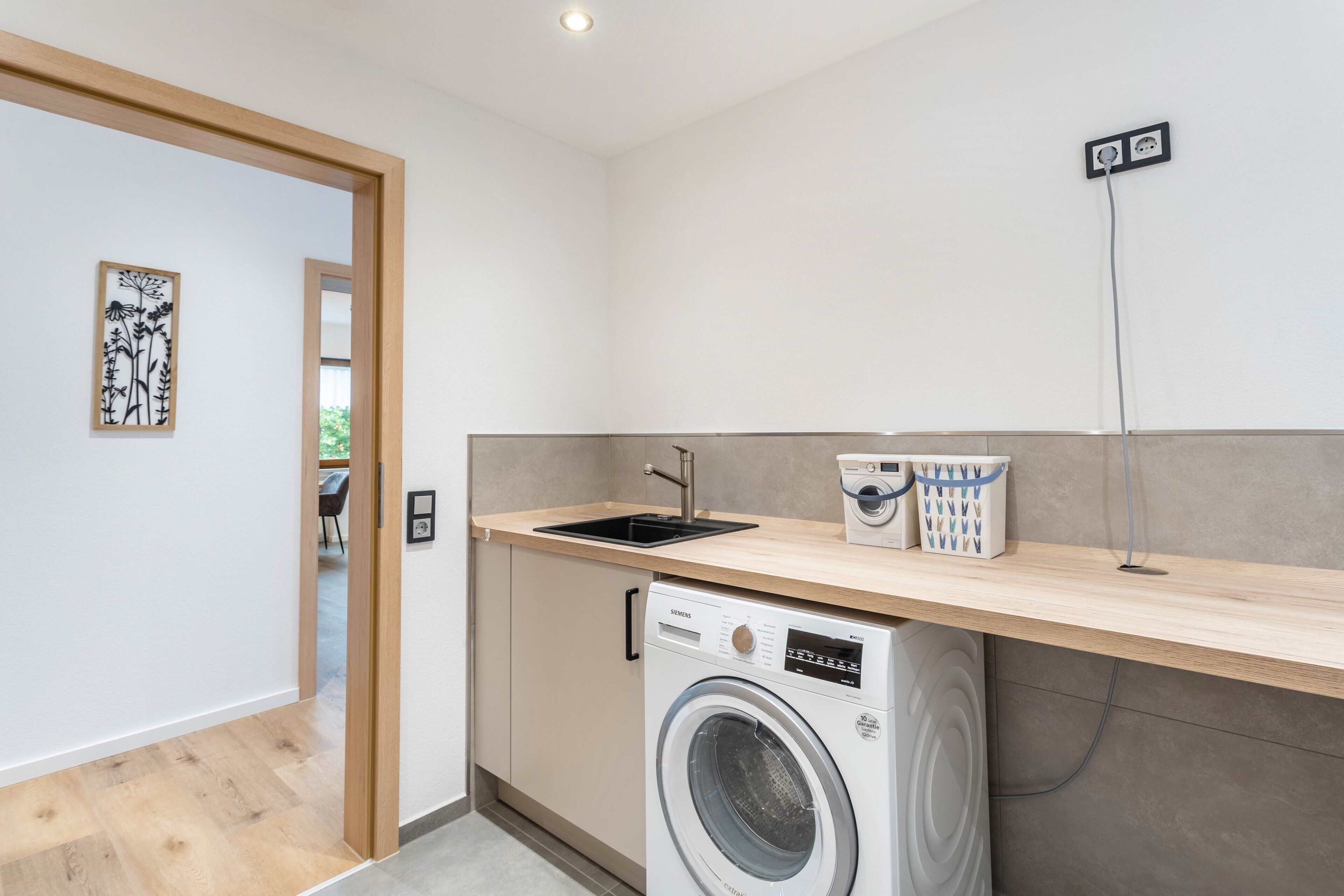 A compact kitchen with a washing machine, a sink, and a countertop with storage baskets.