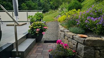 A paved outdoor area with steps leading to a railing, surrounded by various potted plants and flowers.