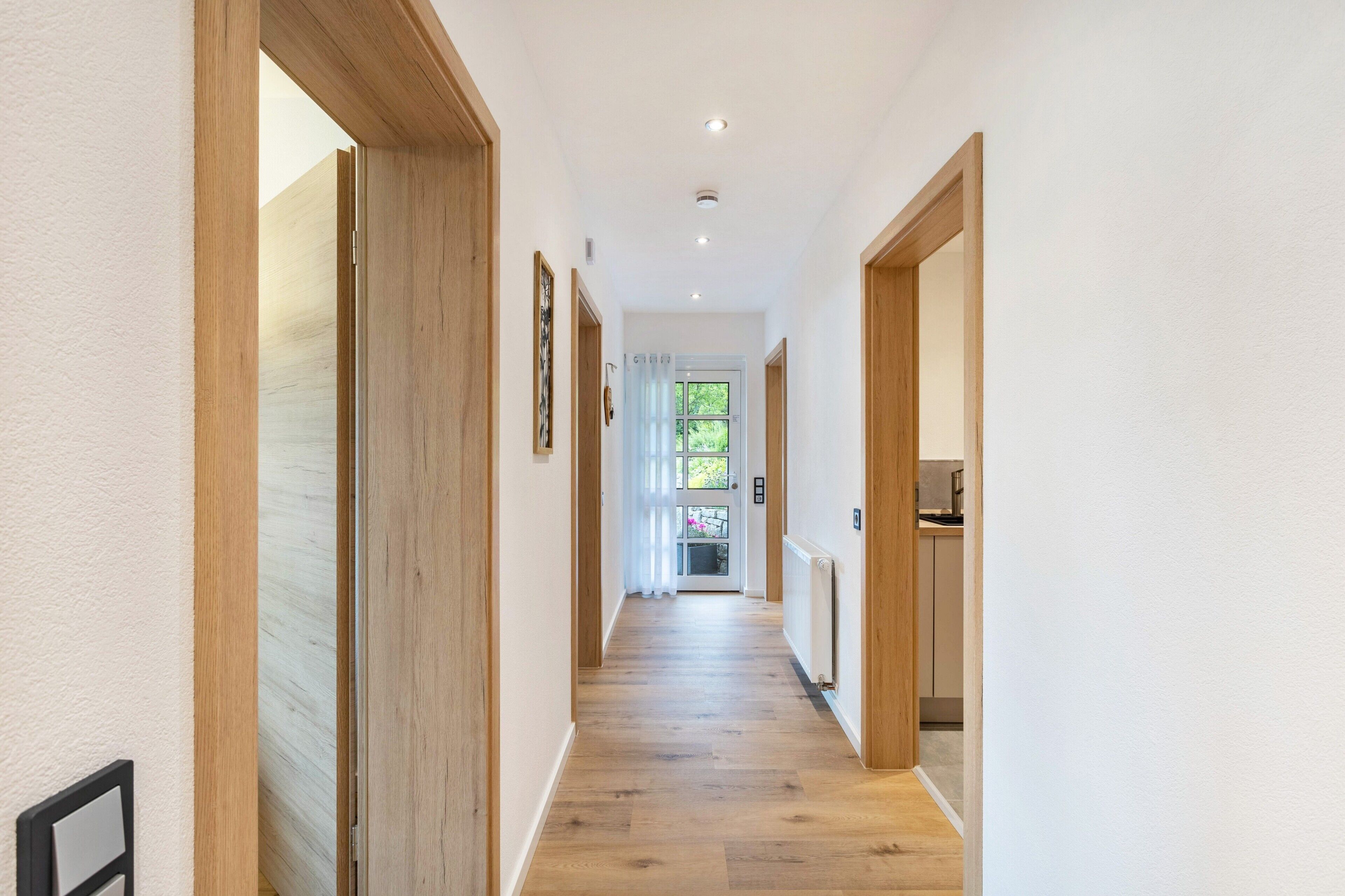 A hallway with wooden doors, a radiator, and a window with a view of greenery.