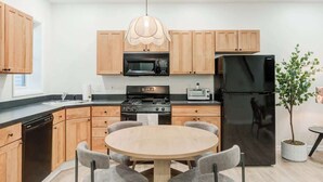 A modern kitchen with wooden cabinets, a black refrigerator, a microwave, a stove, and a dining table with four chairs. - Cozy & Convenient 3-Bedroom Near Washington Square (Philadelphia)