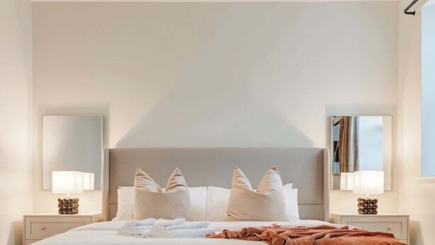 A modern hotel room with a large bed, two bedside tables with lamps, a bench, and a geometric patterned rug. - Cozy & Convenient 3-Bedroom Near Washington Square (Philadelphia)