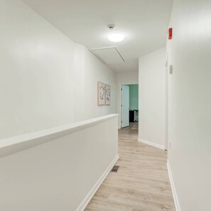 En hall med vita väggar, ett ljust trägolv och en taklampa. I slutet av hallen finns en dörr.