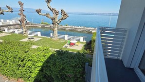 A balcony with a view of a body of water, a tree, and a grassy area with a fence.