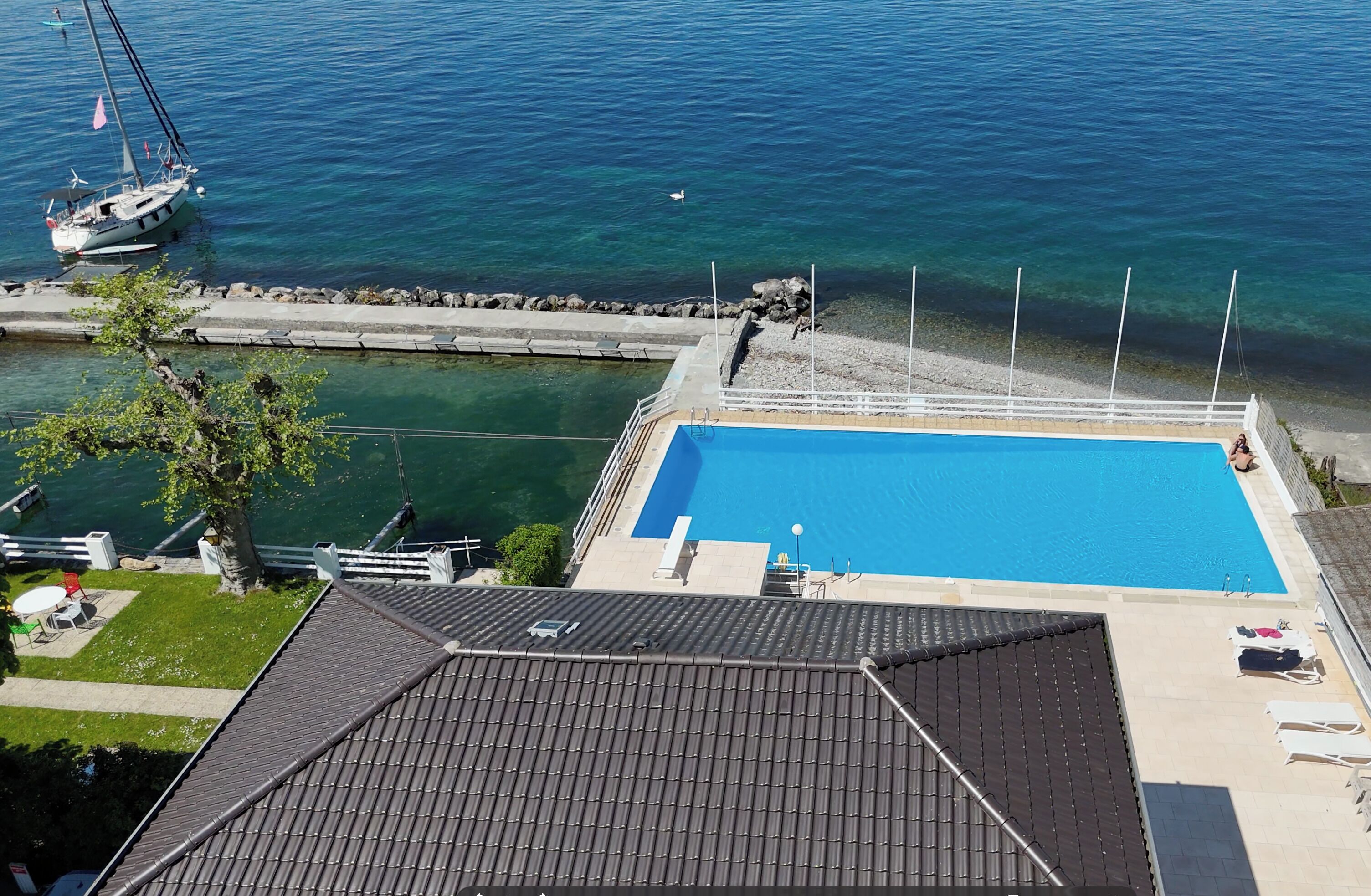 A swimming pool adjacent to a body of water, a boat, and a building with a tiled roof.