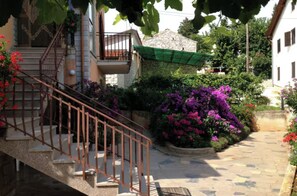 A stone staircase leading to a balcony with a metal railing, surrounded by lush greenery and flowering plants. - Quiet Retreat With Terrace (Umag)
