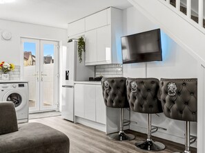 Eine moderne Küche mit Waschmaschine, einem an der Wand befestigten Fernseher und drei Barhocker.