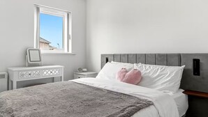 Et moderne soveværelse med en stor seng, et natbord, en sengegavl og et vindue med udsigt.