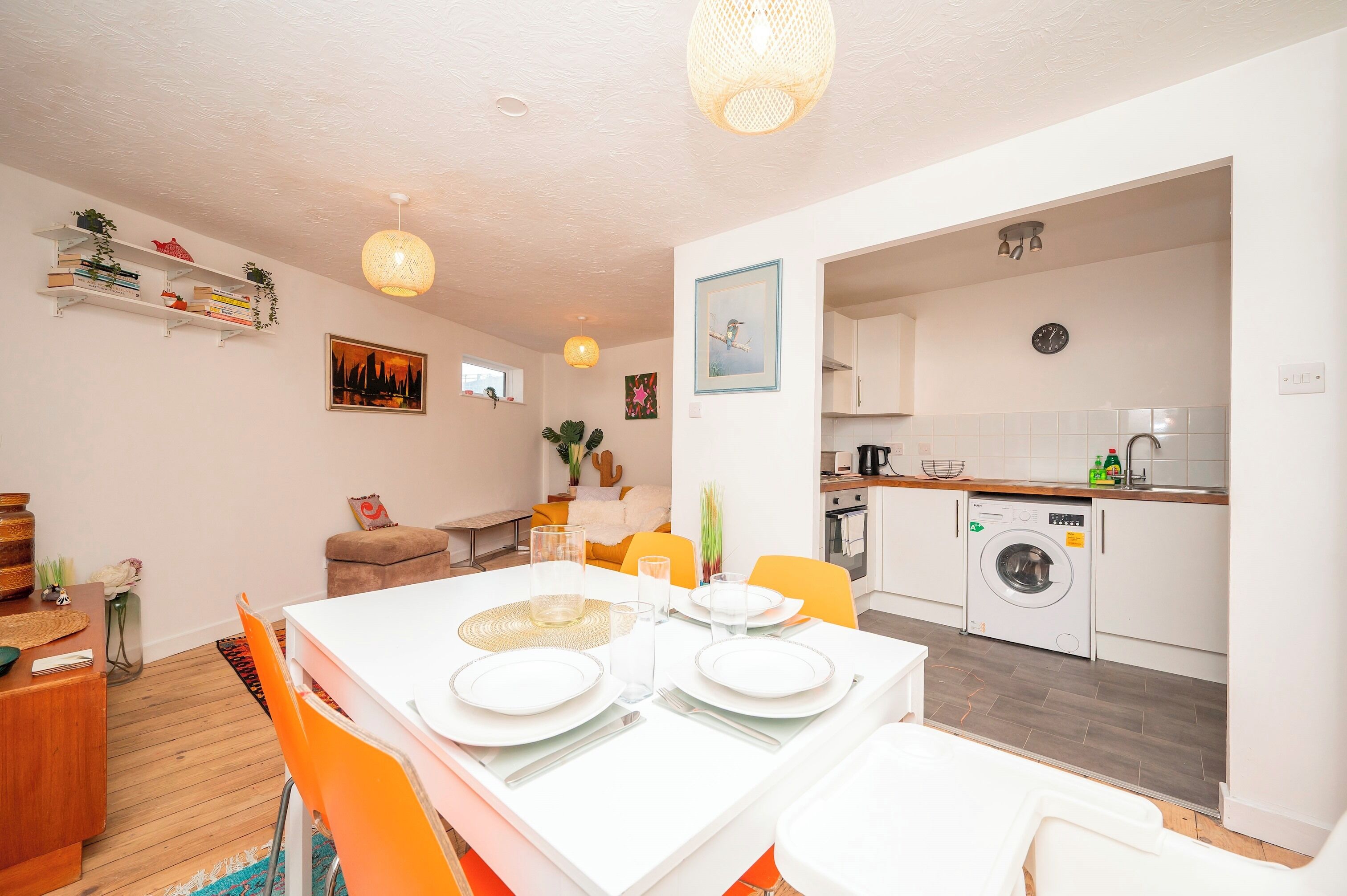 A modern kitchen with a washing machine, a dining area with a table set for two, and a living area with a sofa and a coffee table.