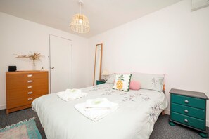 Ein Schlafzimmer mit Bett, Kommode, Nachttisch, Spiegel und einer Pendelleuchte.