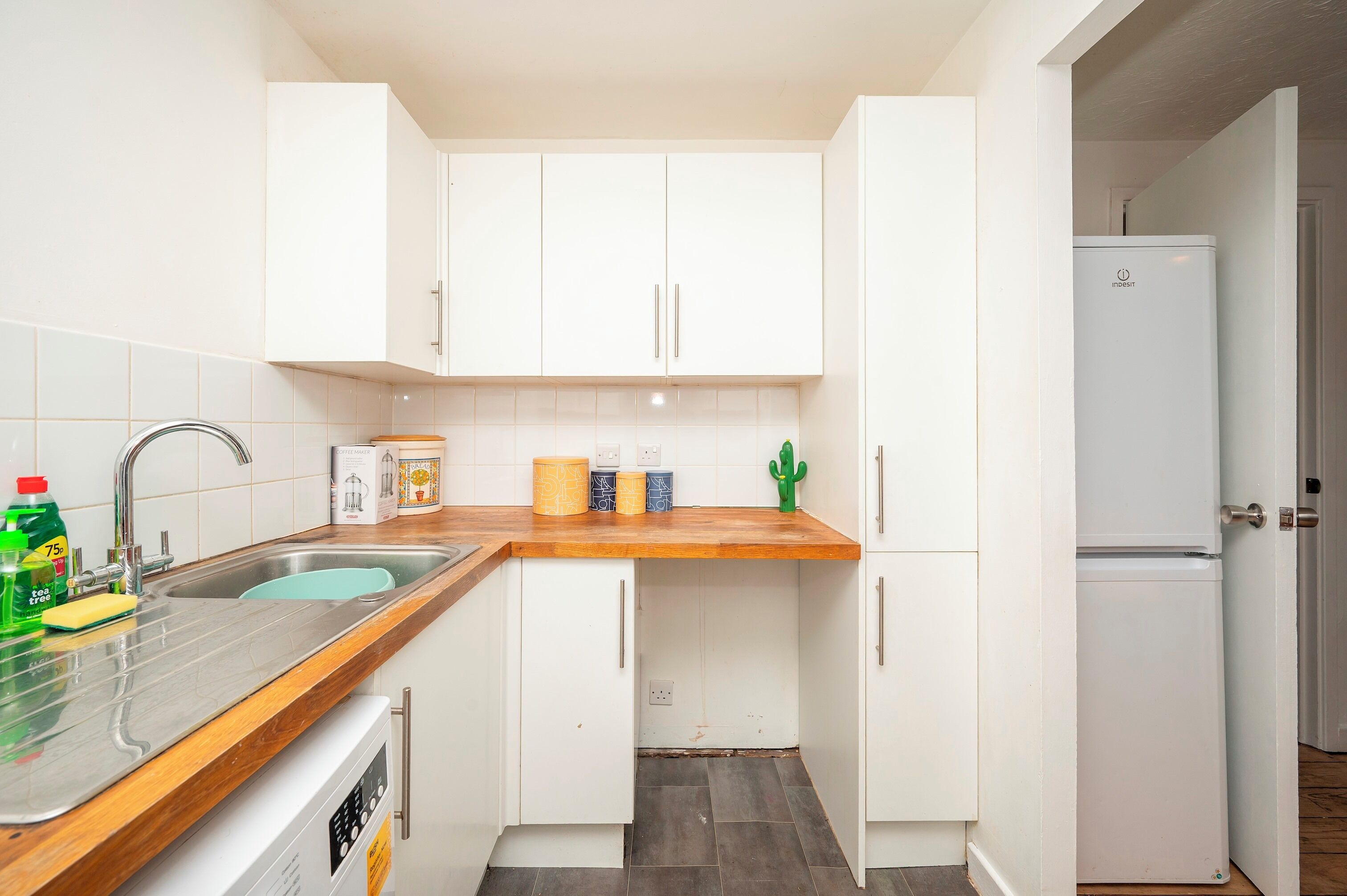 Une cuisine de taille réduite avec des meubles blancs, un plan de travail en bois, un évier en acier inoxydable et un réfrigérateur blanc.