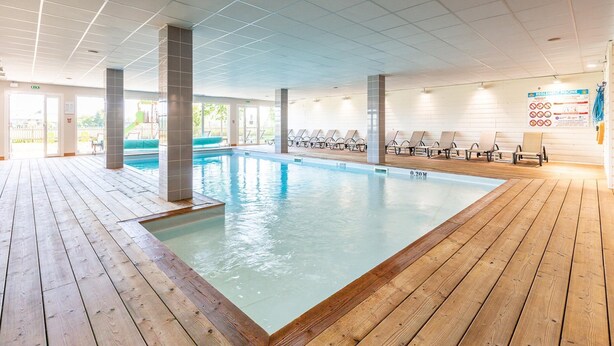 Ein Hallenbad mit Holzterrasse, Liegestühlen und freiem Blick ins Freie.