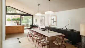 Een moderne keuken met een groot kookeiland, barkrukken, hanglampen en uitzicht door grote ramen.