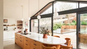 Een moderne keuken met een groot eiland, houten kasten en een eethoek met rieten stoelen.