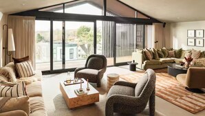 Een ruime woonkamer met een groot raam, een zithoek, een salontafel en een gestreept fauteuil.