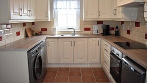 Une cuisine avec des meubles blancs, un lave-linge, un lave-vaisselle et une machine à café.