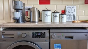Un lave-linge à chargement frontal et une machine à café sur un plan de travail de cuisine.