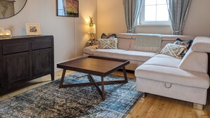 Un salon comprenant un canapé, une table basse, un meuble en bois foncé, un tapis à motifs, une lampe fixée au mur et une fenêtre avec des rideaux.