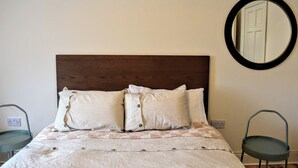 Un lit avec une tête de lit en bois, deux oreillers, une couvre-lit à carreaux et un miroir rond accroché au mur.