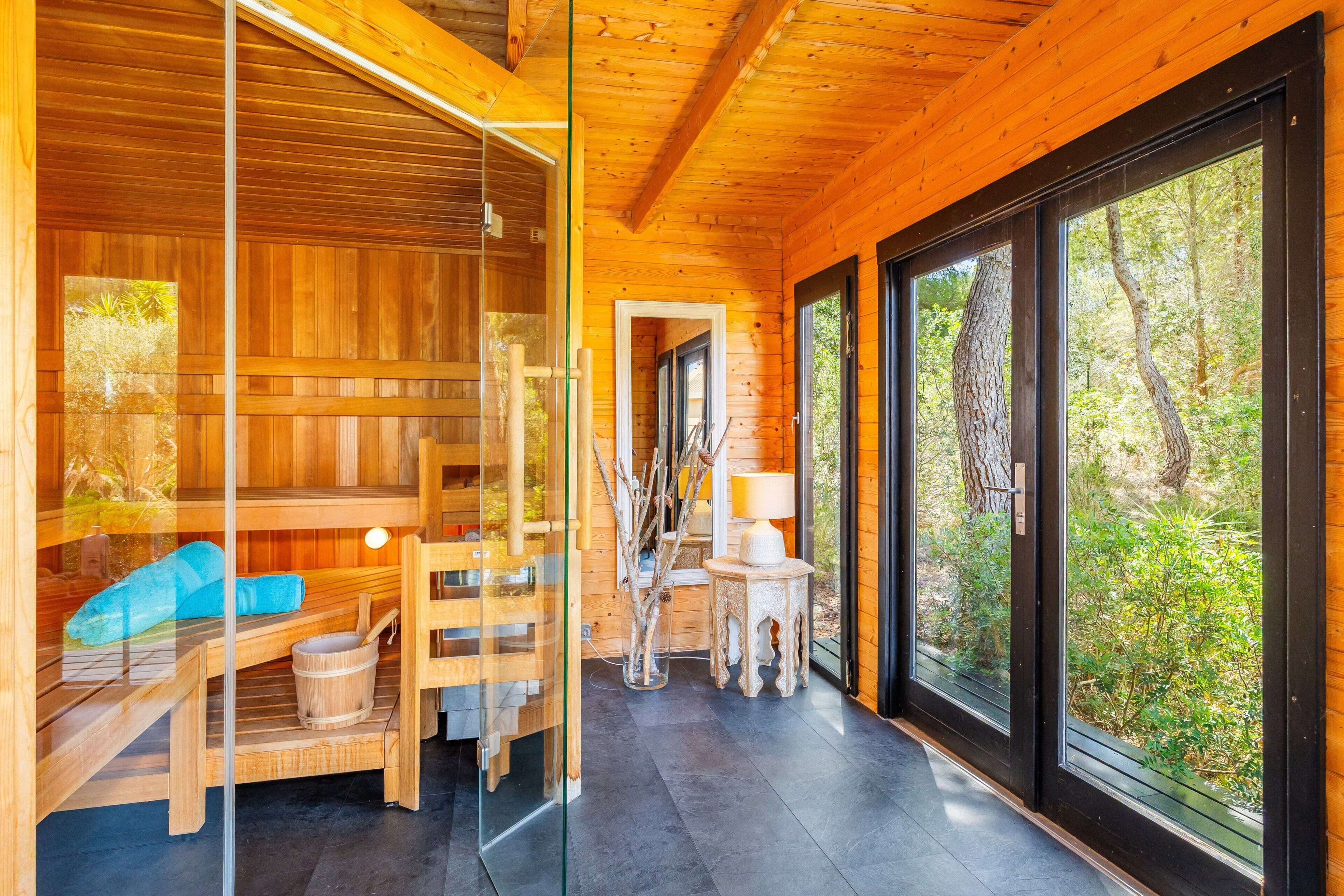 Una cabaña de madera con sauna, una puerta de cristal que da al exterior y vistas al bosque.