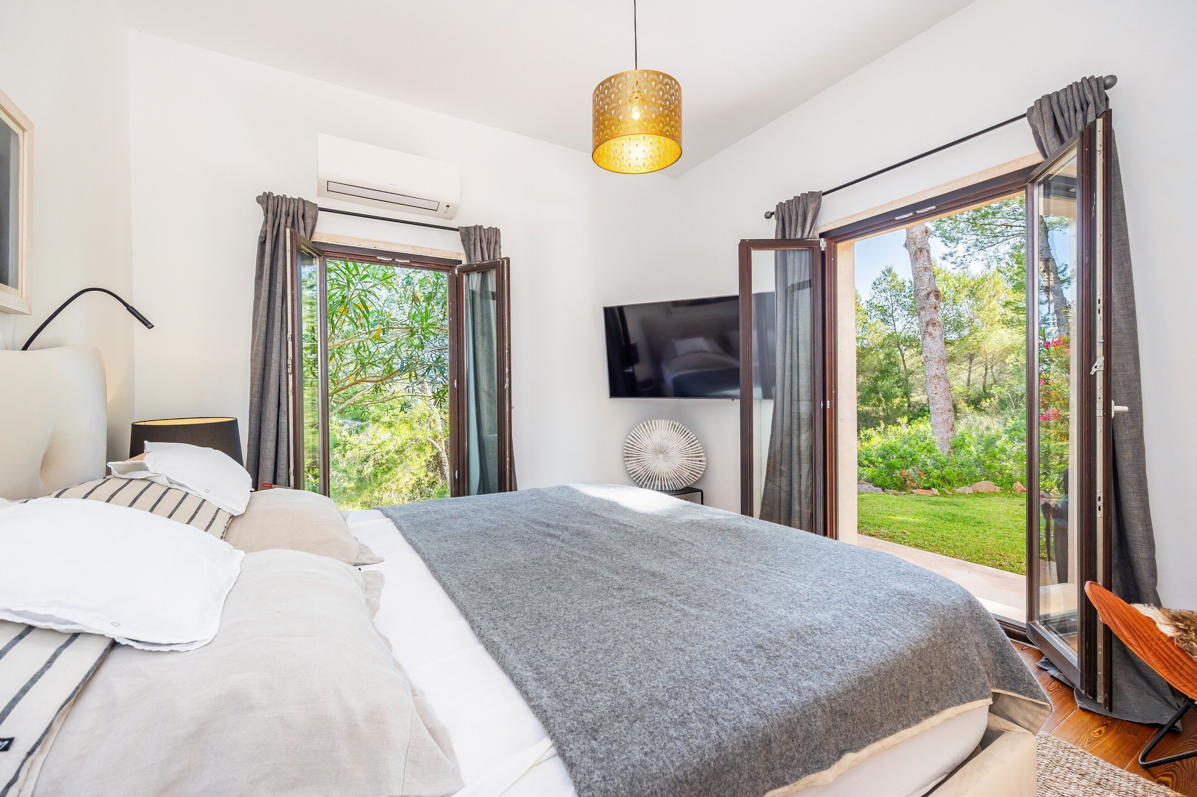 A bedroom with a bed, a TV, a ceiling light, and a sliding glass door to a garden.
