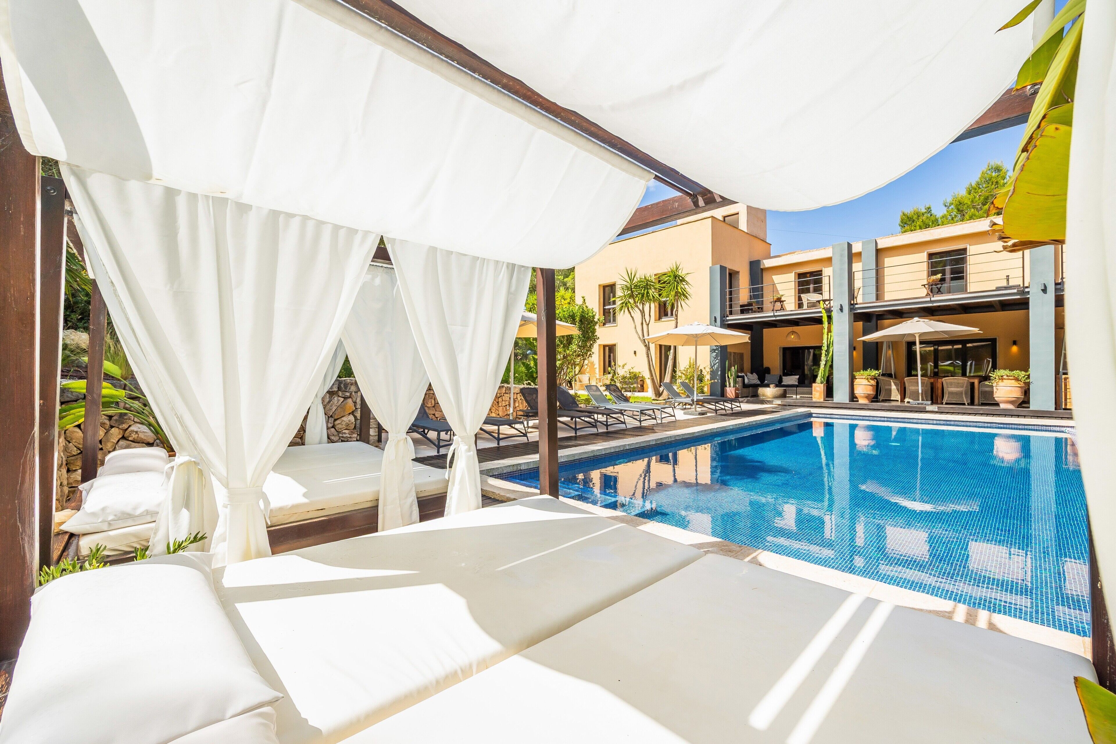 Ein Poolbereich mit weißen Sonnensegeln, Liegestühlen und freiem Blick auf den Pool.