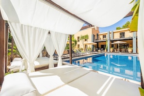 Ein Poolbereich mit weißen Sonnensegeln, Liegestühlen und freiem Blick auf den Pool.