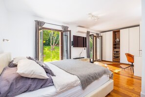 Ein modernes Schlafzimmer mit einem großen Bett, einem Schreibtisch, einem Stuhl, einer Schiebetür, die auf einen Balkon führt, und integrierten Stauraum.