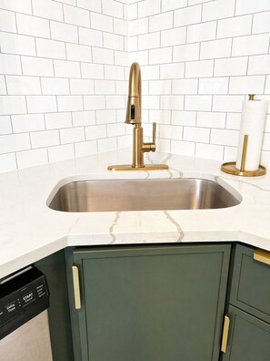 A kitchen with a stainless steel sink, a gold faucet, a white marble countertop, and green cabinets. - Gothic-meets-mid-century 2BR in Lakeview | Statment Kitchen + Dining for 4 (Chicago)