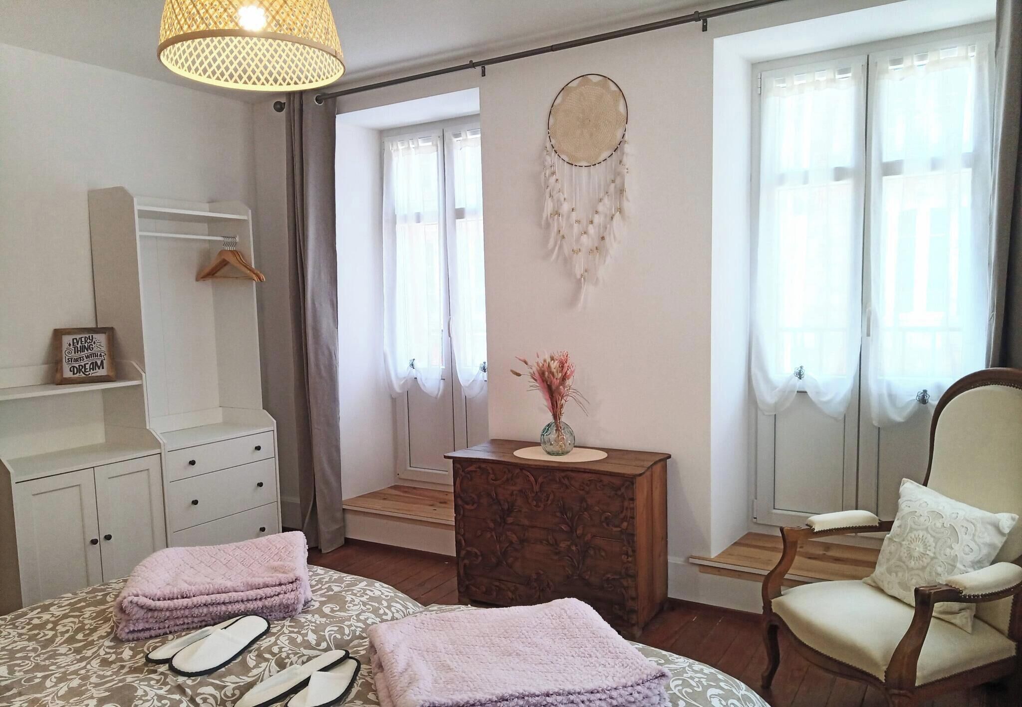Un dormitorio con cama, cómoda, tocador, silla, atrapasueños y ventana con cortinas.