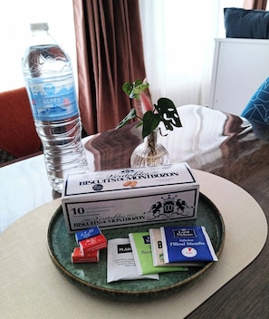 Une chambre d’hôtel avec un lit, une bouteille d’eau, une plante et un plateau contenant des biscuits et des sachets de thé.