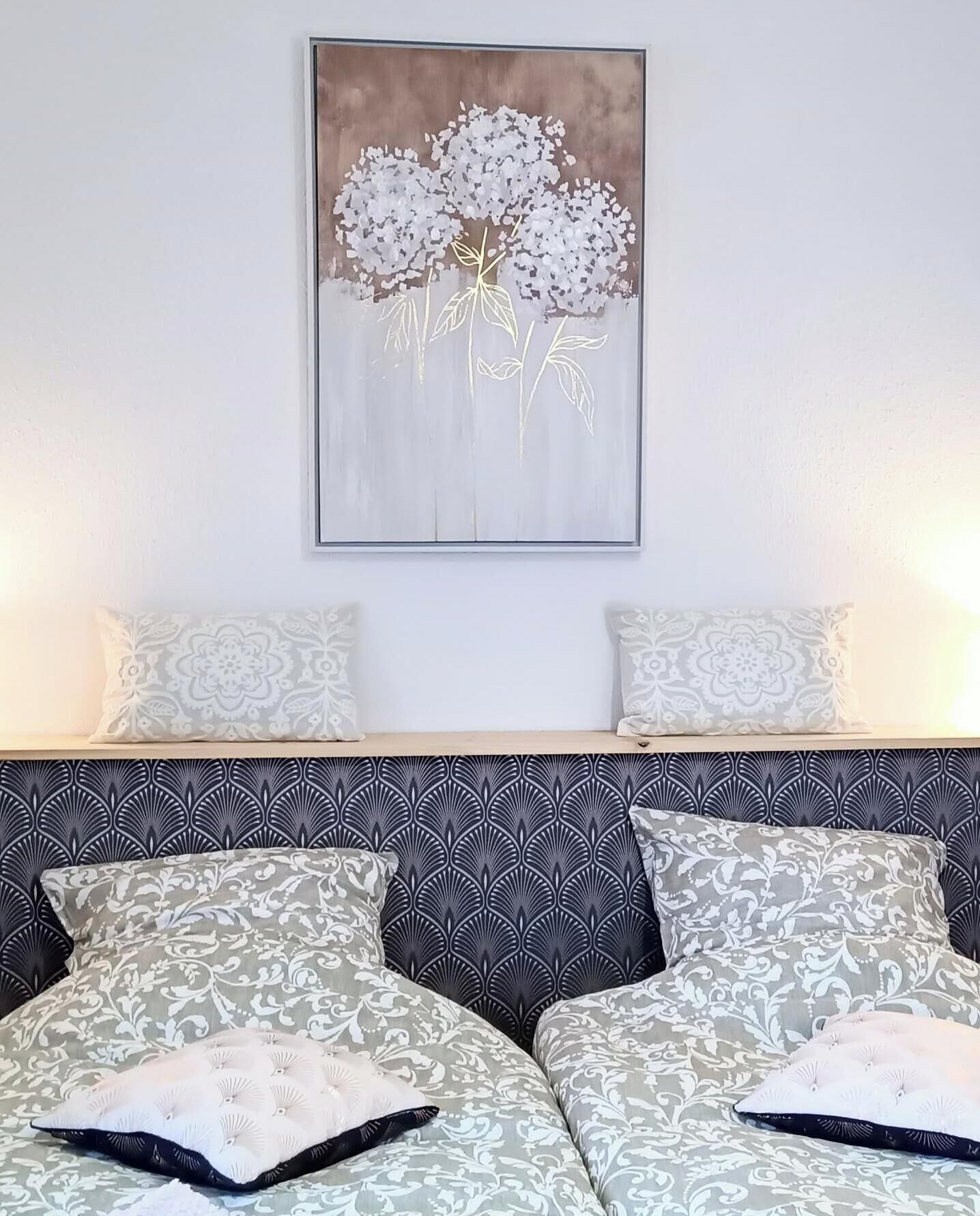 A bedroom with a bed, two pillows, a headboard, and a wall-mounted artwork.