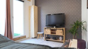 Uma sala de estar moderna com uma televisão sobre um suporte de madeira, um banquinho pequeno e um vaso de planta.
