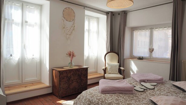 Um quarto com cama, uma cadeira, cômoda, penteadeira e janela.