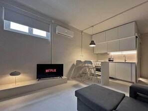 Ein modernes Wohnzimmer mit Flachbildfernseher, einer Couch, einem Essbereich mit Stühlen, einer Küche mit Schränken und einer Klimaanlage.