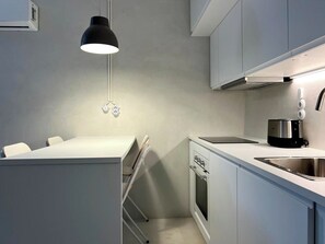 Eine moderne Küche mit weißen Schränken, einem eingebauten Backofen, einem Kochfeld und einer schwarzen Pendelleuchte.
