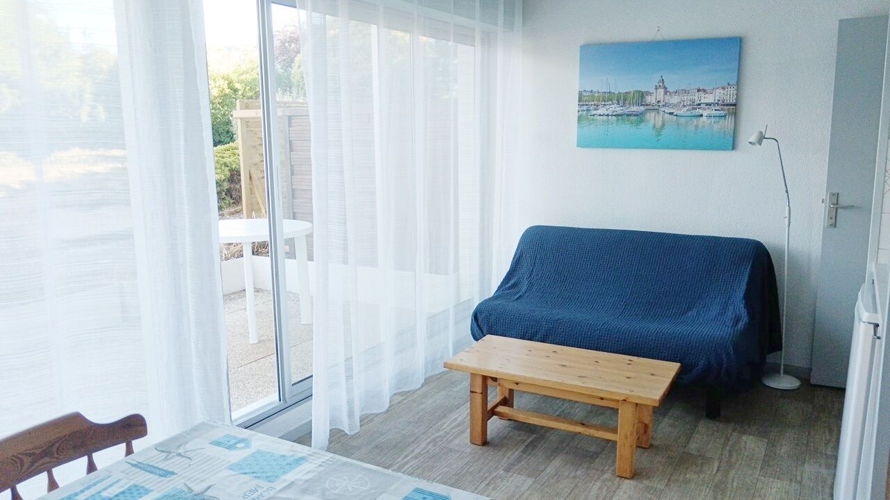 Ein Zimmer mit einem Holztisch, einem blauen Sofa, einem Bild an der Wand und Blick durch eine Glastür.