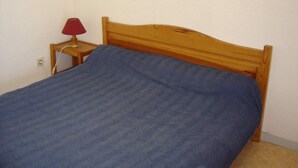 Un lit simple avec une tête de lit en bois, une lampe rouge sur une table de chevet et une couverture bleue.