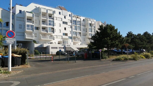 Un immeuble résidentiel à plusieurs étages, doté de balcons, d’un espace de stationnement et d’un panneau indiquant qu’il est interdit de se garer.