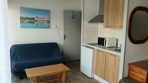 Une pièce de taille modeste comprenant un canapé, une petite table, une kitchenette équipée d’un four à micro-ondes et une porte donnant sur une autre pièce.