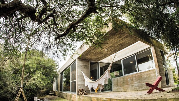 A modern house with large windows, a hammock, and a red chair outside.