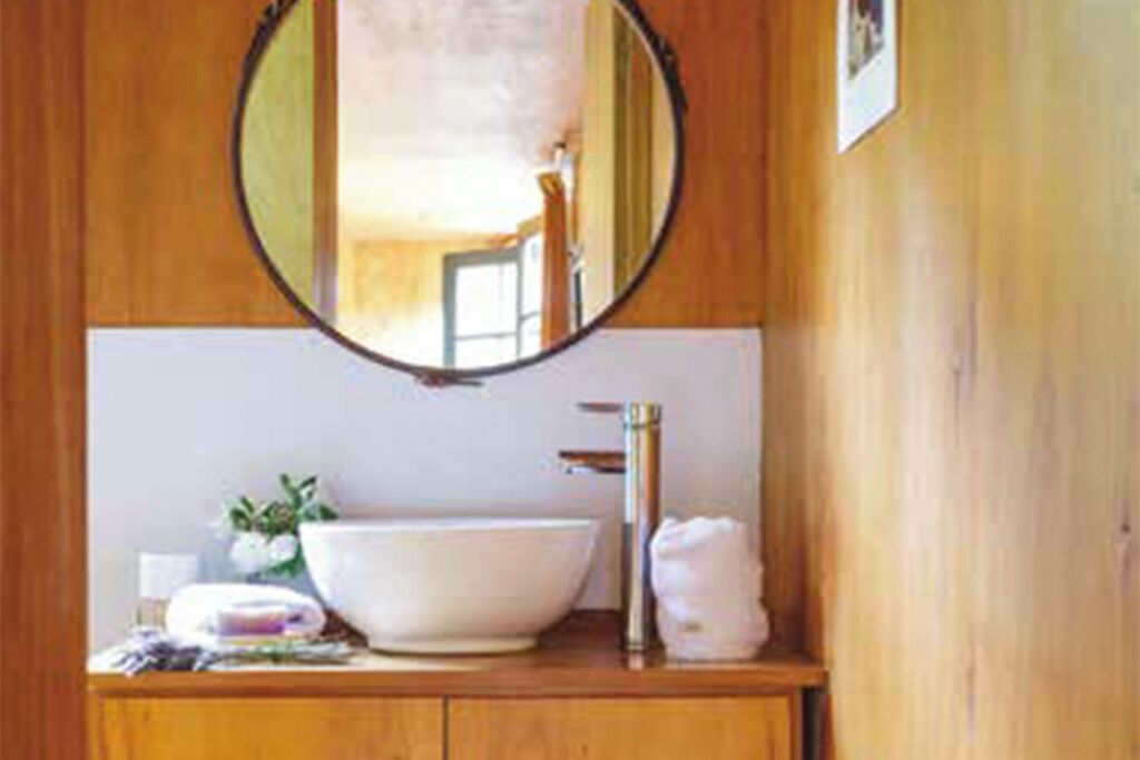 A bathroom with a wooden vanity, a round mirror, a white sink, and a towel.