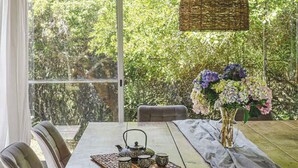 A dining table with chairs, a vase with flowers, and a teapot set on a placemat.