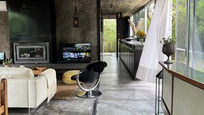 A modern living room with a fireplace, a sofa, a television, and a large window with a view of greenery.