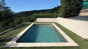 Una piscina rettangolare con acqua cristallina e blu, circondata da erba sintetica e una bassa muratura in cemento.