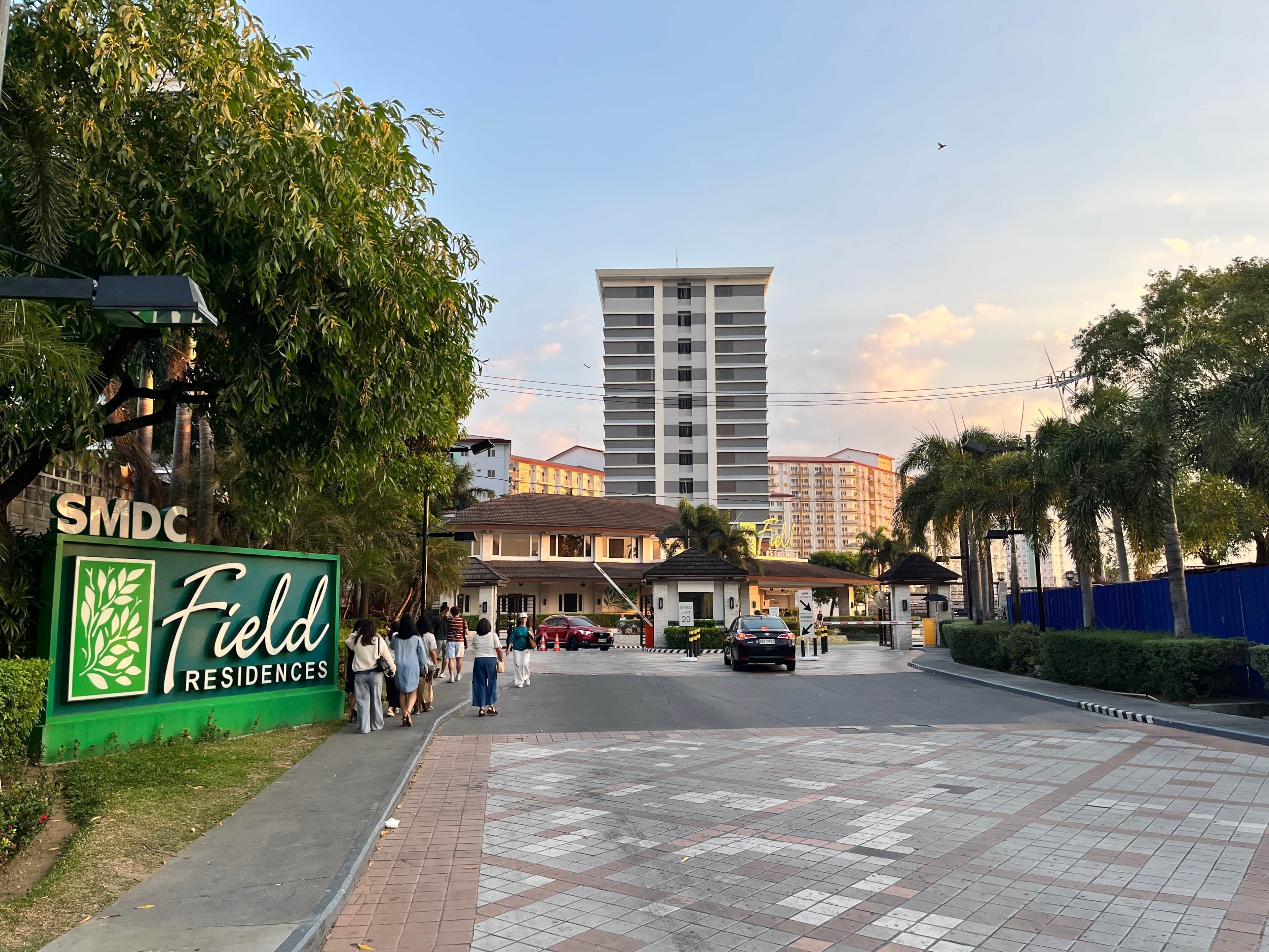 A residential area with a sign for Field Residences, a paved walkway, and a tall building in the background.