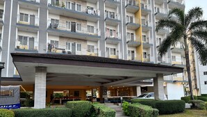 Un hotel de varios pisos con un vestíbulo cubierto, balcones y una palmera.