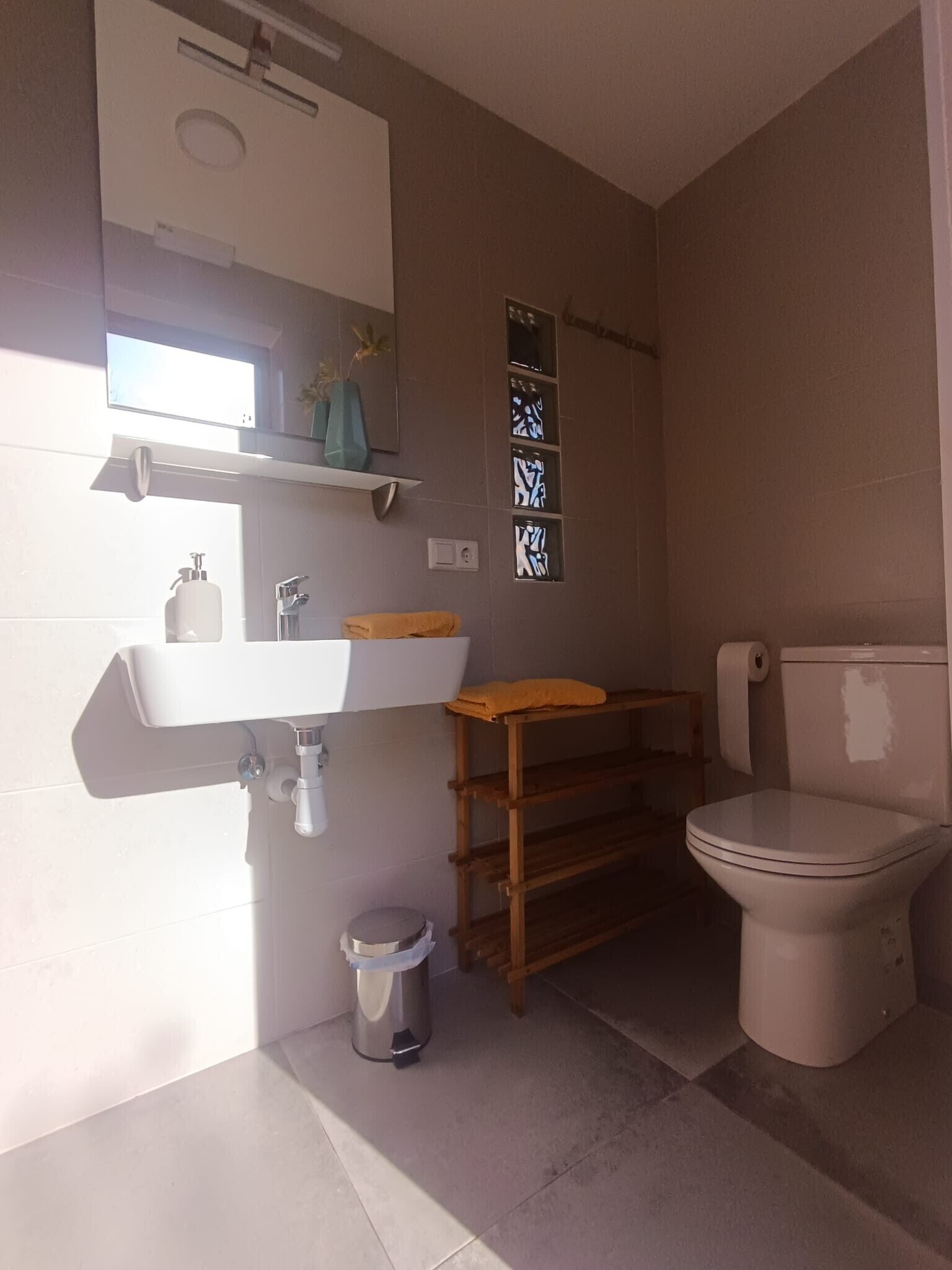 Un baño con lavamanos blanco, espejo, inodoro y un pequeño cubo de basura.