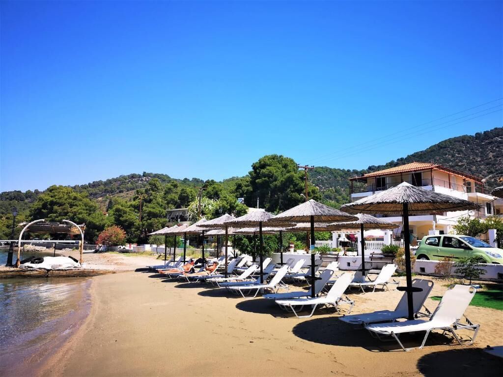 A beach with sun loungers and umbrellas, a clear sky, and a building in the background.
